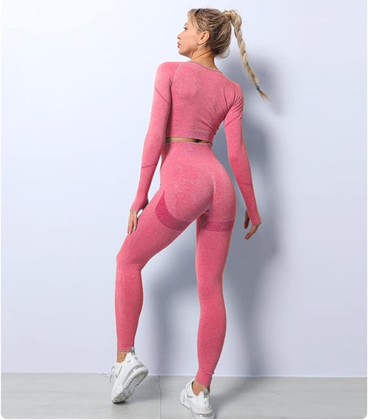 Een vrouw in een roze yoga-trainingsset en witte sneakers poseert met haar rug naar de camera en kijkt over haar schouder.