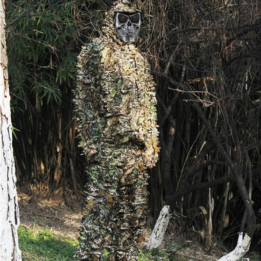 Persoon die een Ontdek het ultieme camouflagepak draagt - Ghilliekostuum met een schedelmasker, staande in een bosrijke omgeving.