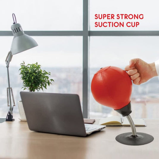 Bij een laptop op een tafel staat iemand te slaan op een rode desktopboksbal met een supersterke zuignapvoet, effectief hand-oogcoördinatie oefenend en de voordelen ervarend van het