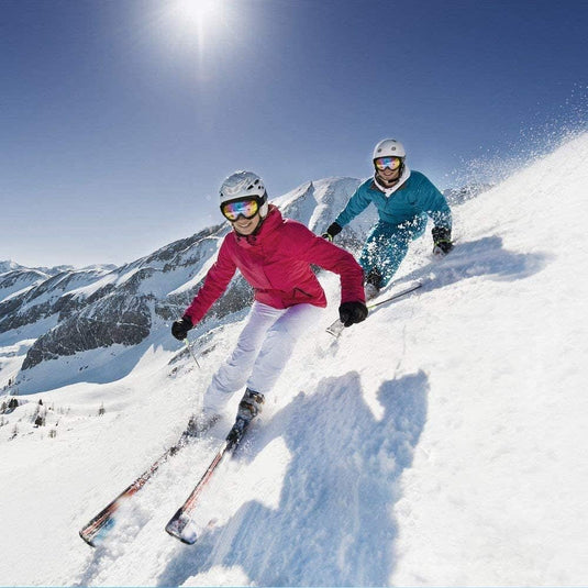 Twee skiërs glijden op een heldere dag van een besneeuwde berghelling af, gekleed in de Bescherm je ogen en genieten van de wintersport met deze hoogwaardige sneeuwbrillen.