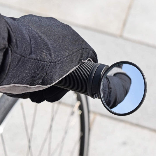 Zin bij de productnaam: Een gehandschoende hand verstelt de BM-45 stuureinde fietsspiegel op een fietsstuur, waarbij veiligheid en zichtbaarheid centraal staan.