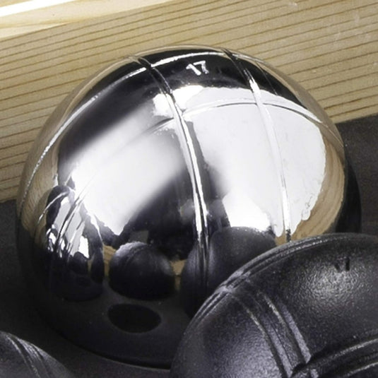 Close-up van een metalen petanquebal die de omgeving weerspiegelt, zittend naast andere zwarte ballen in een Houten Kist.