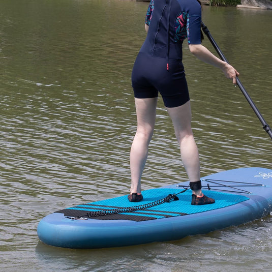 Een persoon in een wetsuit die aan het paddleboarden is op een kalm meer, waarbij hij zich concentreert op het balanceren terwijl hij een lange peddel gebruikt om door het water te navigeren, beveiligd met de veiligste manier om van het water te genieten.