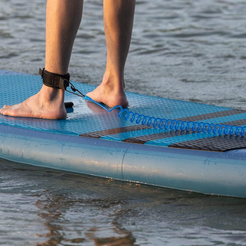Laad afbeelding in Galerijviewer, Close-up van de voeten van een persoon op een stand-up paddleboard met een daaraan bevestigde de veiligste manier om van het water te genieten rond één enkel, staande in ondiep water.

