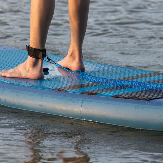 Close-up van de voeten van een persoon op een stand-up paddleboard met een daaraan bevestigde de veiligste manier om van het water te genieten rond één enkel, staande in ondiep water.