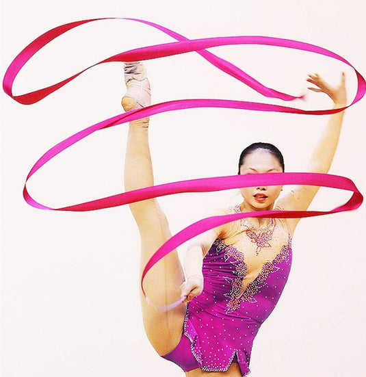 Een ritmische turnster voert een hoge beengreep uit terwijl ze een Betoverende danslinten manipuleert in een spiraalvormig patroon rond haar lichaam, wat artistieke expressie laat zien.