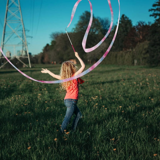 Een jong meisje met blond krullend haar speelt met Dansbanden voor kinderen voor ritmische gymnastiek op een zonnig grasveld.