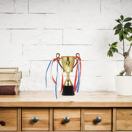 De perfecte gouden trofee voor jouw prestaties met rode en blauwe linten, geplaatst op een houten tafel naast een stapel boeken en een duurzaam gepotte