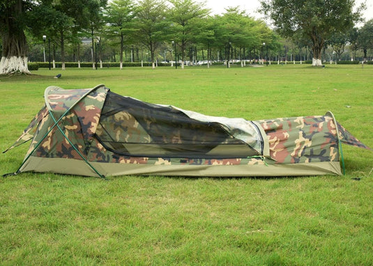 Een BIVY-tent opgezet op groen gras in een park met bomen op de achtergrond.