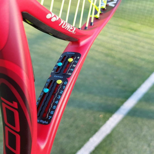 Een close-up van een rood racket toont het Draagbaar tennis scorebord, waarop de punten en games op een groene baan worden bijgehouden.