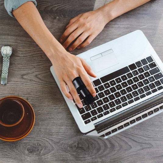 De handen van een persoon worden op het toetsenbord van een laptop geplaatst, terwijl een horloge en een kopje op het bureau staan. Aan de ene kant valt de Beste vingerspalk voor herstel en verlichting op.