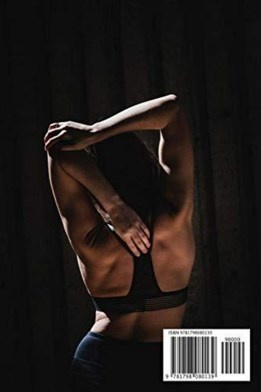 In een slecht verlichte ruimte strekt iemand in een sportbeha zijn arm achter zijn rug uit. Dit legt de geest van fitness vast die te zien is in de