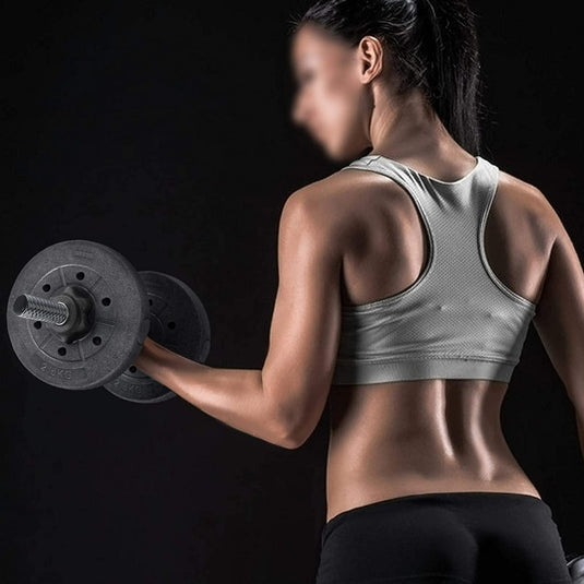 Een vrouw in sportkleding tilt een verstelbare halterset van 20 kg voor krachttraining thuis, geconcentreerd op haar training, tegen een donkere achtergrond.