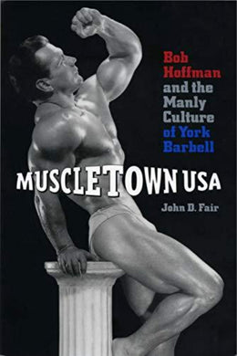 Omslag van het boek 'John D Fair: Muscletown USA: Bob Hoffman and the Manly Culture of York Barbell (Engels) (Paperback)' met een gespierde man die poseert op een voetstuk, wat de erfenis van York Barbell op het gebied van gewichtheffen symboliseert.