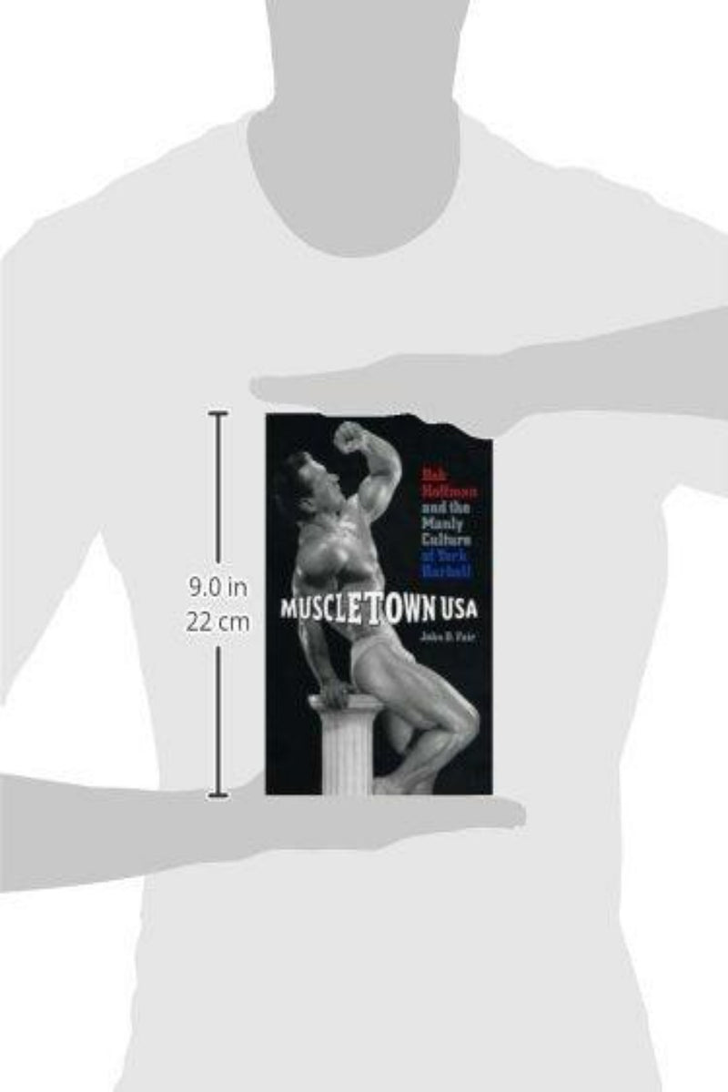 Laad afbeelding in Galerijviewer, Een grafisch T-shirt met de boekomslag van &quot;John D Fair: Muscletown USA: Bob Hoffman and the Manly Culture of York Barbell&quot; van John D. Fair, met een zwart-wit afbeelding van een bodybuilder die op een voetstuk poseert.
