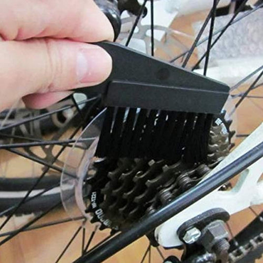 Een hand met een zwarte borstel en de Houd je fietsketting in topconditie met onze professionele fietsketting reinigingsset om de versnellingscassette van een fiets schoon te maken.