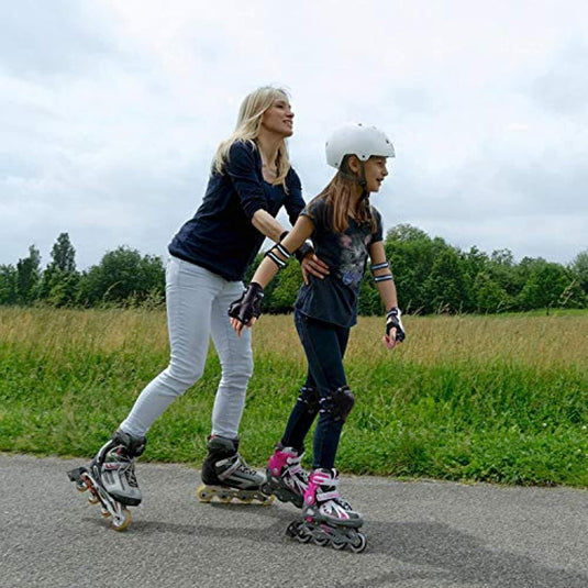 Een vrouw en een jong meisje met helmen en optimale skeelerbescherming skeelerend op een pad buiten.