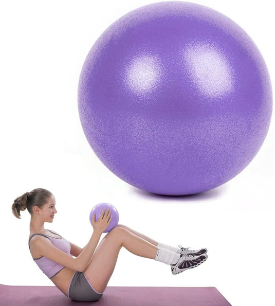 Een vrouw in trainingsuitrusting voert flexibiliteitsoefeningen uit met een kleine paarse kleine Pilates-bal, zittend op een mat naast een grote paarse oefenbal.