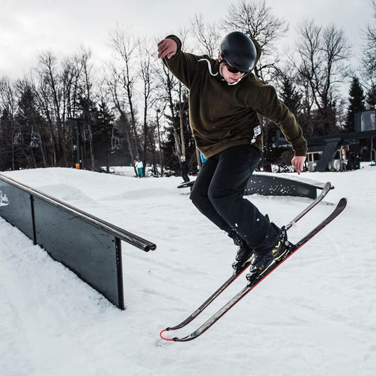 Een leer je kinderen skiën terwijl ze een grind uitvoeren op een rail in een besneeuwd terreinpark.