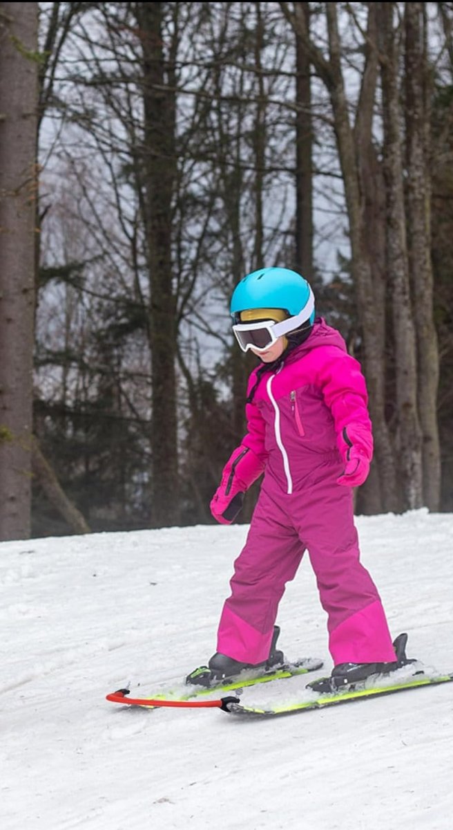 Laad afbeelding in Galerijviewer, Een persoon in een roze skipak en blauwhelm die aan het skiën is op een besneeuwde heuvel met bomen op de achtergrond, en laat zien hoe Leer je kinderen skiën effectief met deze skitipconnector werkt.
