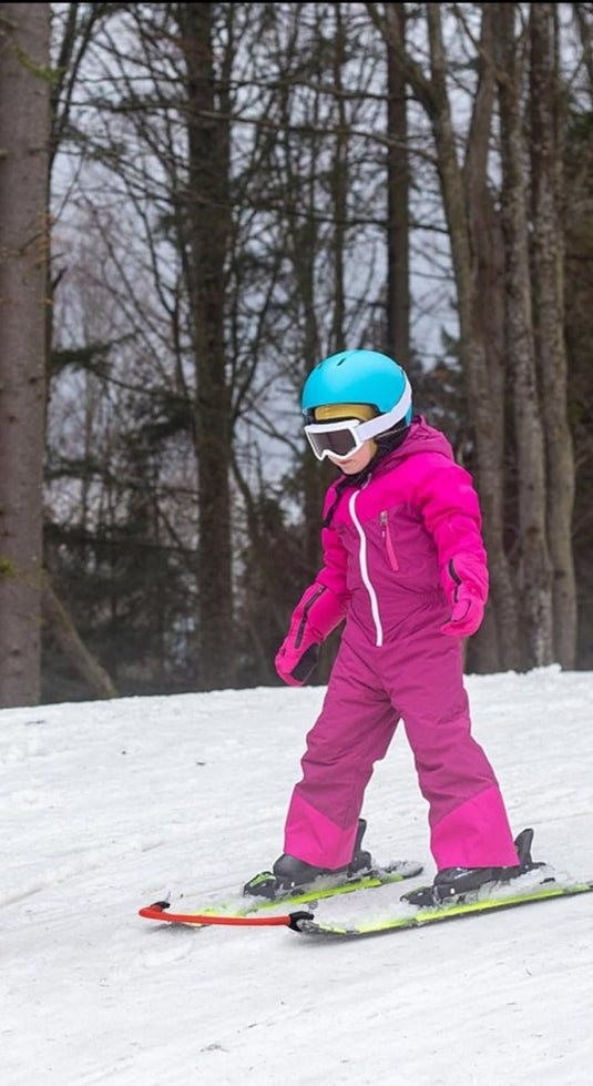 Een persoon in een roze skipak en blauwhelm die aan het skiën is op een besneeuwde heuvel met bomen op de achtergrond, en laat zien hoe Leer je kinderen skiën effectief met deze skitipconnector werkt.