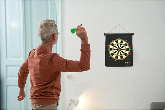 Senior man speelt binnenshuis met een dubbelzijdig magnetisch dartbord.