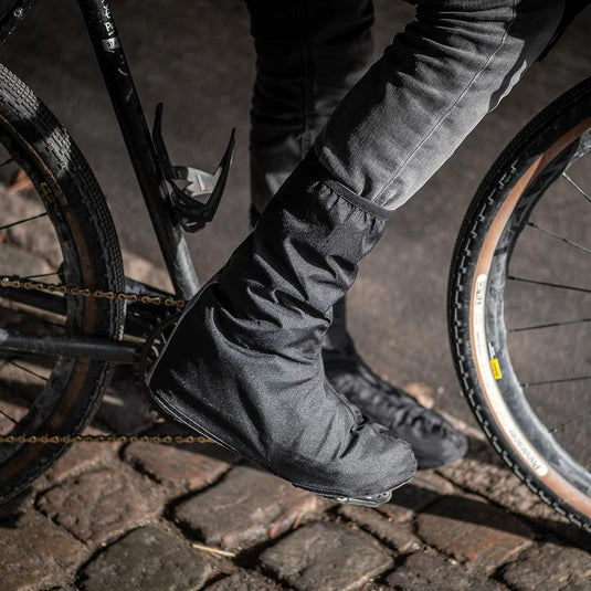 Fietser draagt Regenoverschoenen voor fietsers om schoenen te beschermen tijdens het fietsen met waterdichte schoenbeschermers.