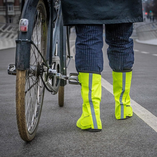 Een persoon met mogelijke veiligheid draagt heldergele reflecterende regenoverschoenen voor fietsers, staande naast een fiets op een stads- Regenoverschoenen voor fietsers: blijf droog en stijlvol.