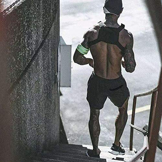 Een gespierde man met tatoeages loopt een trap op, met een pet op, Ontdek het ultieme comfort en de functionaliteit van onze heren 2-in-1 shorts en sneakers. Het beeld heeft een stenig stedelijk gevoel.