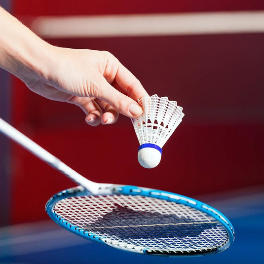 Een hand die een LED-verlichte badmintonshuttle vasthoudt boven een badmintonracket tegen een wazige rode en blauwe achtergrond.