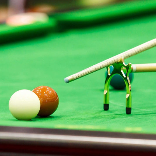 Een close-up van een Snooker tafelsteunen met een keu geplaatst in een keubruggenset, gericht op een witte en een bruine bal.