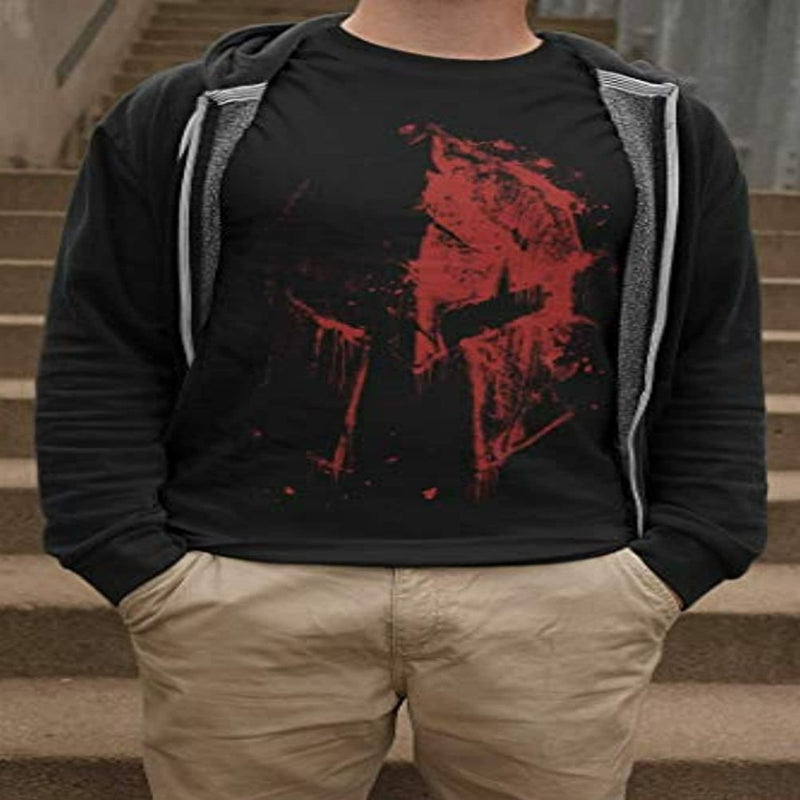 Laad afbeelding in Galerijviewer, Een persoon die een zwart Duik in de wereld van de spartaanse krijgers T-shirt draagt met een rode abstracte print, gelaagd onder een grijze hoodie, gecombineerd met een beige broek, staande op een trap.

