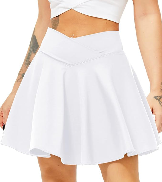 Een vrouw houdt de zoom van haar Tennisrok met broek vast en daaronder een korte broek, waardoor het ontwerp goed zichtbaar is. Ze draagt een witte crop-top en heeft zichtbare tatoeages op haar armen.