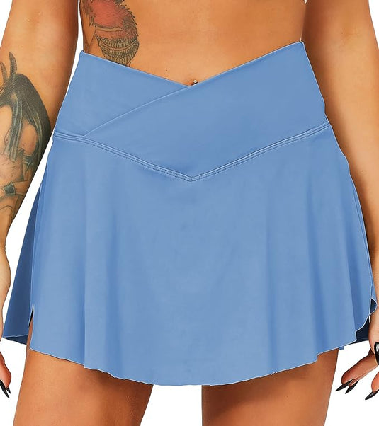 Een close-up van een vrouw die een blauwe Tennisrok met broek draagt, waardoor het diagonale ontwerp wordt benadrukt, met een tatoeage zichtbaar op haar linkerbovenarm.