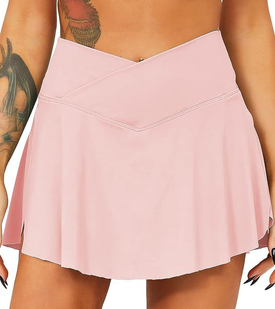 Een close-up van een persoon die een roze Tennisrok met broek draagt. Details omvatten een zichtbare tatoeage op de linkerbovenarm.