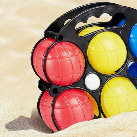 Een set kleurrijke Beleef het plezier van bocciaballen in de kleuren rood, geel en blauw, opgeborgen in een zwart draagrek, geplaatst op een zandstrand voor een jeu de boules-spel.