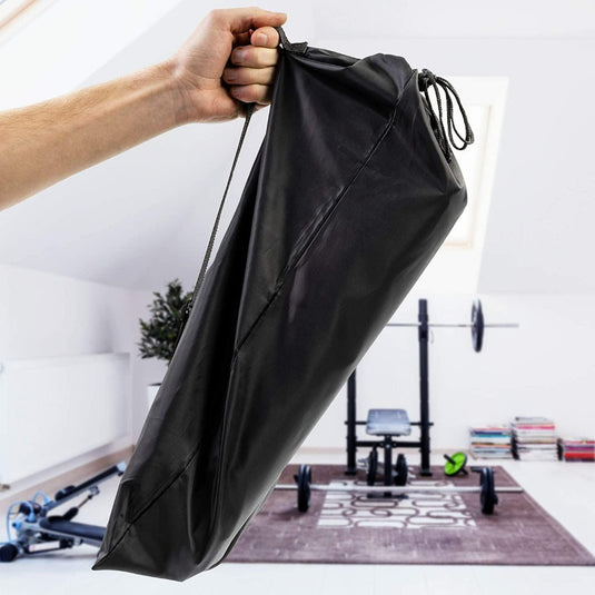 Een hand die een opgevouwen zwarte sporttas vasthoudt in een fitnessruimte met op de achtergrond de Voetbal trainingsmaterialen set - Verbeter je spel.