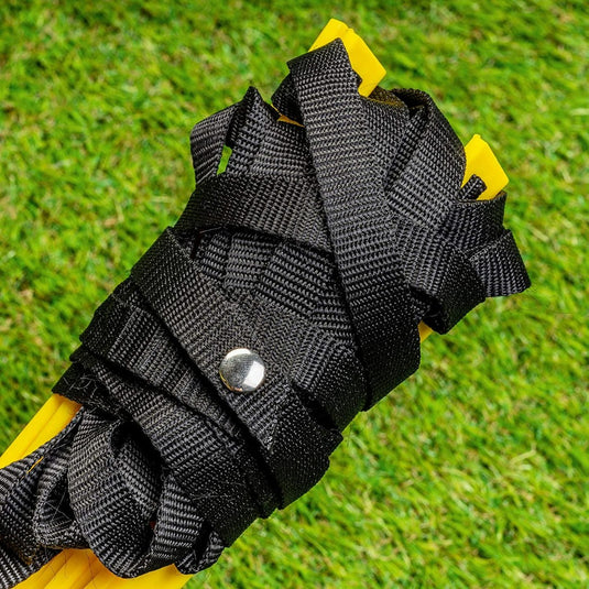Een close-up van een zwart geweven bandje met metalen drukknoop, bevestigd aan een Voetbal trainingsmaterialen set - Verbeter je spel, mogelijk sportuitrusting, tegen een met gras begroeide achtergrond.