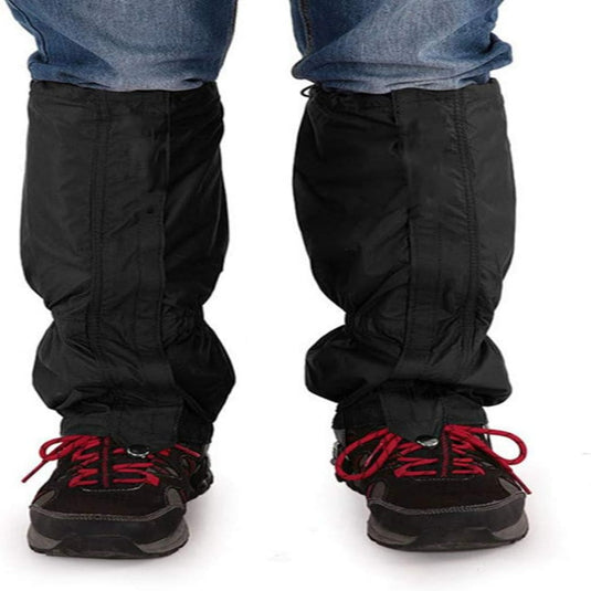 Persoon die de ultieme bescherming voor al je buitenactiviteiten in zwart draagt over een spijkerbroek en zwarte wandelschoenen met rode veters, staande met de voeten iets uit elkaar.