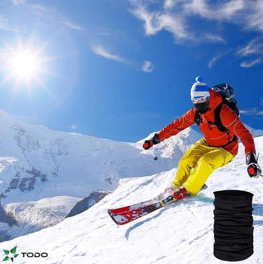 Een skiër in felgekleurde kleding daalt een besneeuwde helling af onder een helderblauwe hemel en draagt onze universele nekhoes.