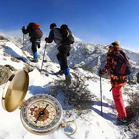 Drie wandelaars die met rugzakken een besneeuwde berg beklimmen, gebruikmakend van trekkingstokken, met op de voorgrond het Happygetfit zakkompas voor buitennavigatie.