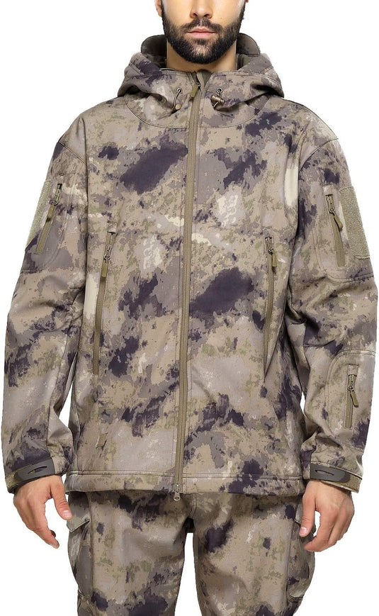 Een man, gekleed in een camouflage tactische heren softshell jas en bijpassende broek, staand met een neutrale uitdrukking.