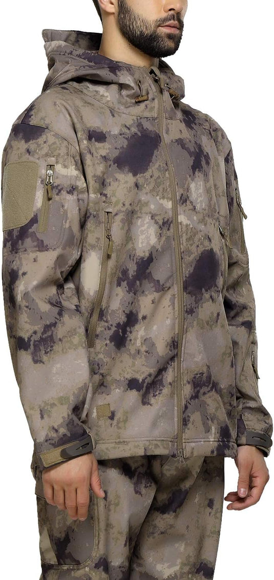 Staande man in zijprofiel, gekleed in een camouflage tactische heren softshell jas en broek met meerdere zakken met ritssluiting.