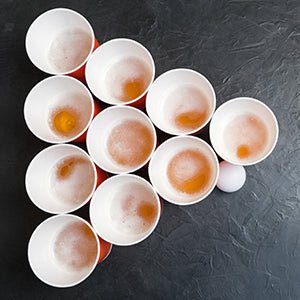 Laad afbeelding in Galerijviewer, Op tafel staan in een driehoek tien kopjes, elk met een drankje. Naast de onderste rij ligt een pingpongbal klaar, perfect voor bierpong met deze veelzijdige set: Speel, daag uit en knutsel met deze handige set van 100 bierpongballetjes!.
