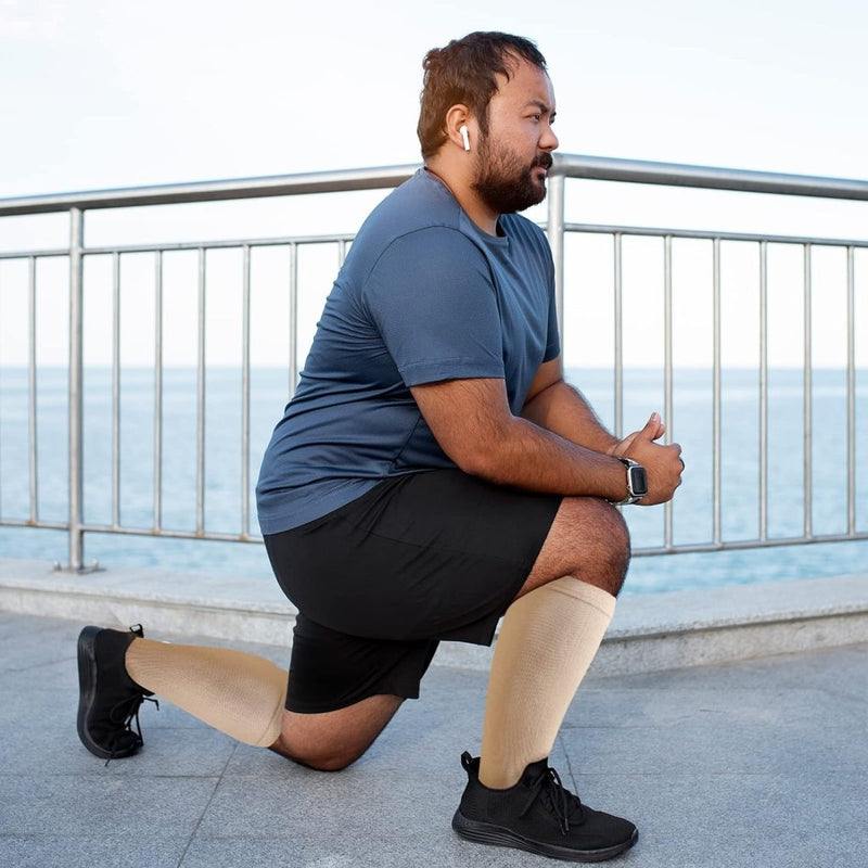 Laad afbeelding in Galerijviewer, Een man in sportkleding knielt aan de waterkant, met een koptelefoon en een smartwatch op. Met &quot;Verbeter prestaties en herstel met compressiesokken voor dames en heren - Maat S/M tot 7XL!&quot; op zijn benen richt hij zich op spierherstel en het verbeteren van zijn bloedsomloop voor optimale prestaties.
