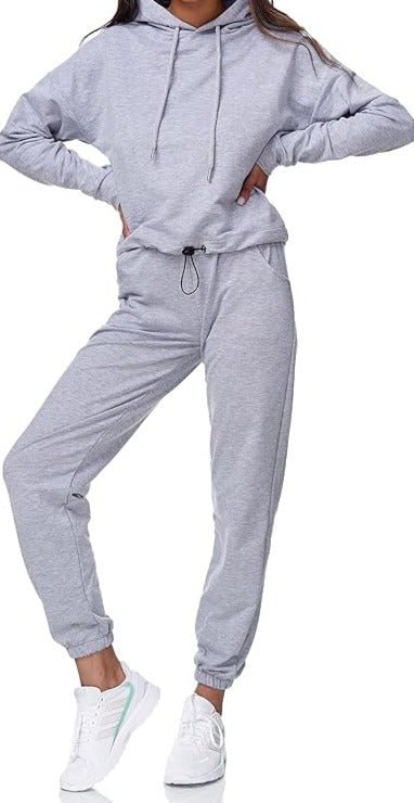 Een persoon in een grijs "Dames joggingpak: Comfort en stijl in één" met een comfortabele pasvorm en witte sneakers poseert stijlvol, één been licht gebogen.