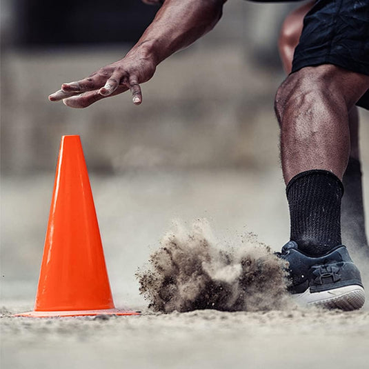 Een atleet in sneakers en zwarte sokken rent langs een trainingskegel en doet stof opwaaien tijdens de voetbaltraining met onze premium trainingskegels.