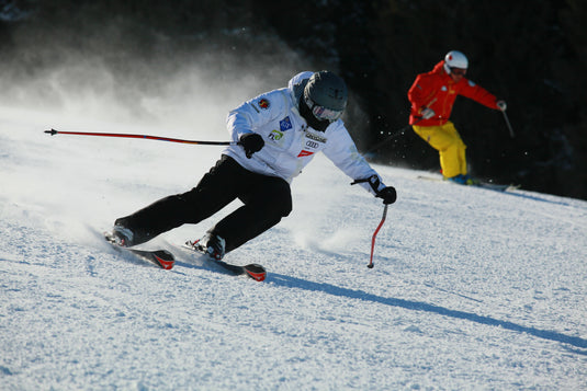 Twee mensen skiën een besneeuwde helling af.