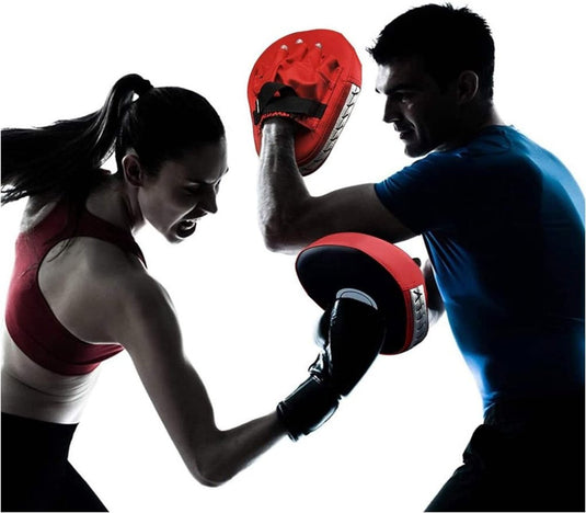 Een man draagt een blauw shirt en gebruikt de duurzame leren focus pads van "Verbeter je training", terwijl een vrouw in bokshandschoenen een stoot uitdeelt tegen het rode oppervlak tijdens een vechtsporttrainingssessie.