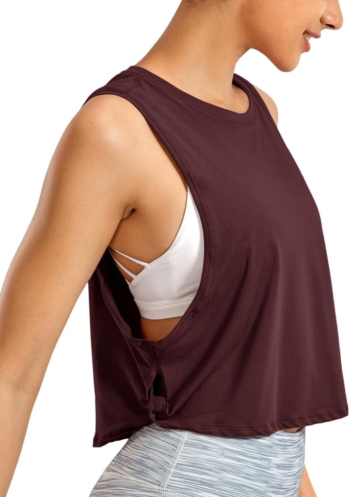 Laad afbeelding in Galerijviewer, Een persoon draagt een stijlvolle kastanjebruine Yoga dames pima katoenen workout tanktop met een knoop aan de zijkant over een witte sportbeha, gecombineerd met een lichtgrijze broek.
